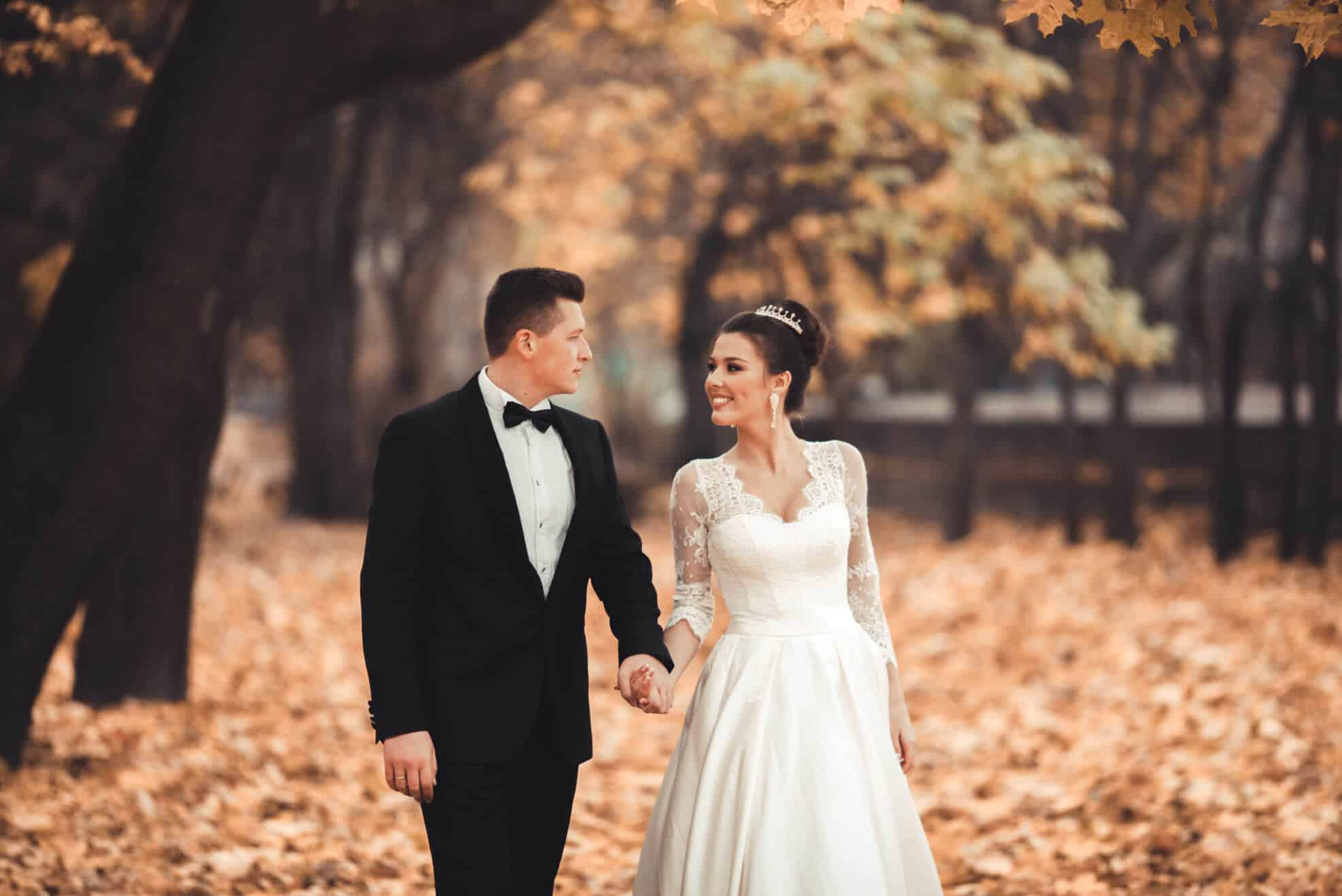 a bride and groom holding hands while walking outside in autumn